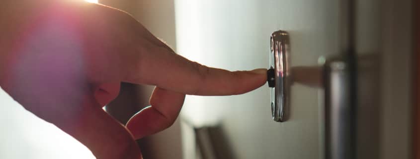 Finger pressing doorbell in sunny apartment building corridor. Close up of male hand ringing door bell in a block of flats. Salesman, fundraiser, guest or visitor behind door.